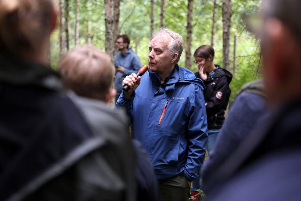 Person presents with other people in birch forest. Photo.