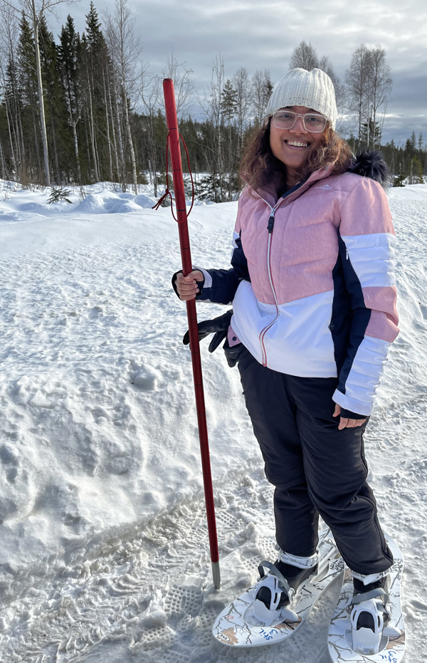 Kvinna i snöskor och termokläder i soligt vinterväder. Foto.