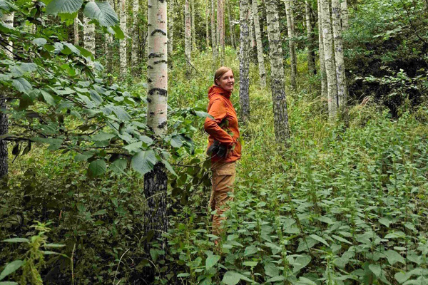 Kvinna i orange jacka står i lövskog. Foto.