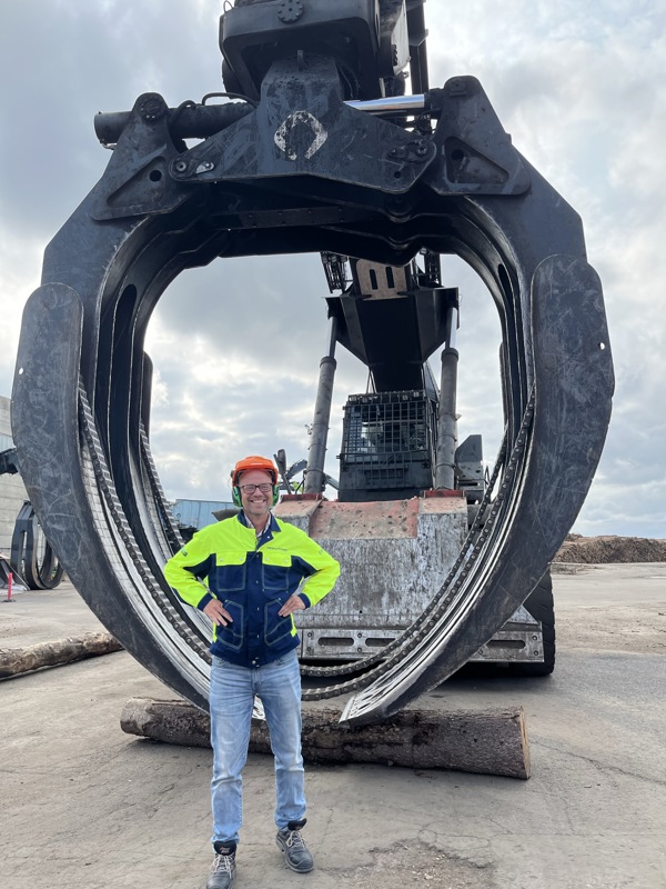 Person standing in front of huge grapple loader. Photo.